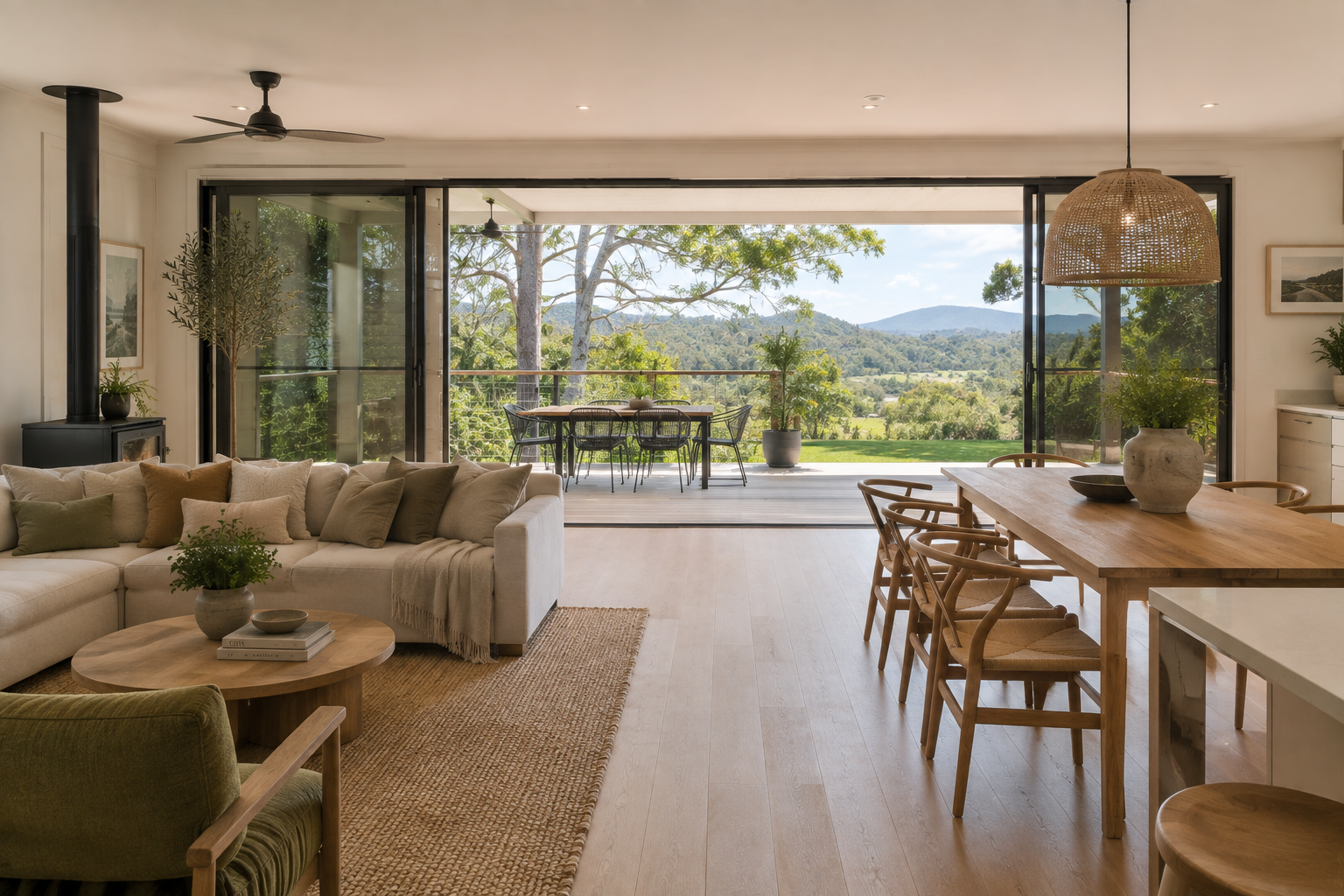Open-plan living and dining area with timber furniture, linen sofa and bi-fold doors opening to a deck with hinterland views