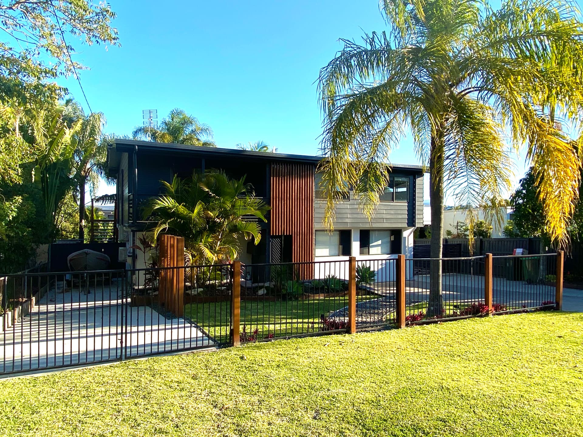 Renovated coastal home facade with white render, timber posts and native planting